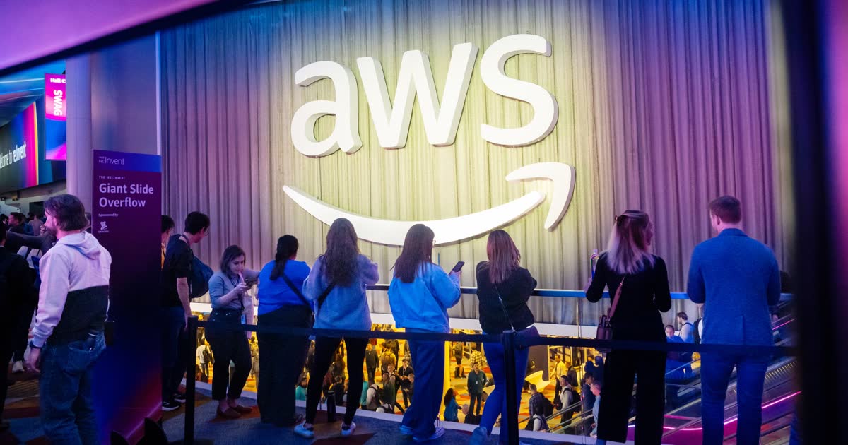 Amazon Q3 earnings cover: visitors at the AWS re:Invent conference stand beneath a large lit AWS logo